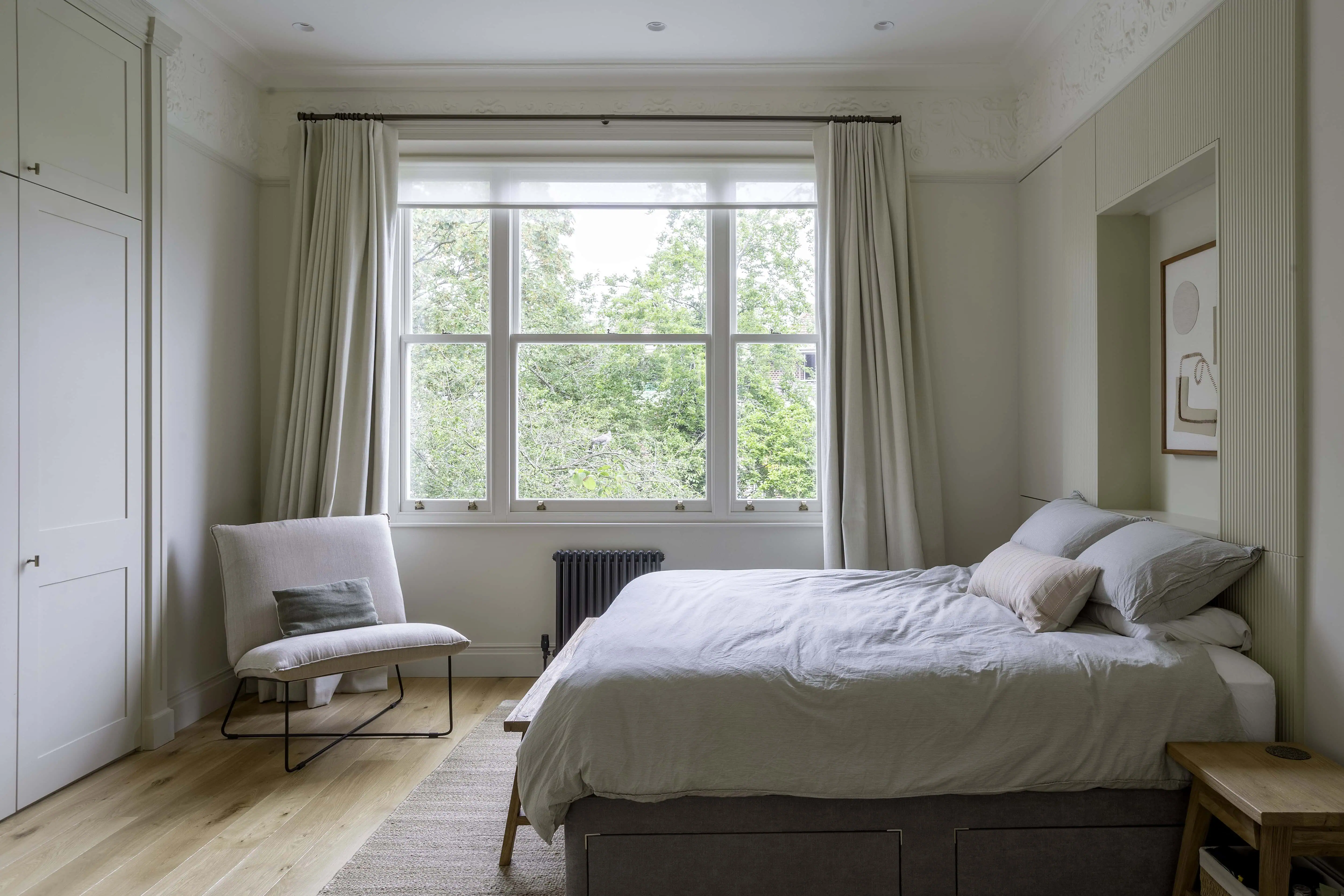 Principal bedroom featuring bespoke headboard joinery, garden views, and Victorian architectural details in a renovated Belsize Park flat