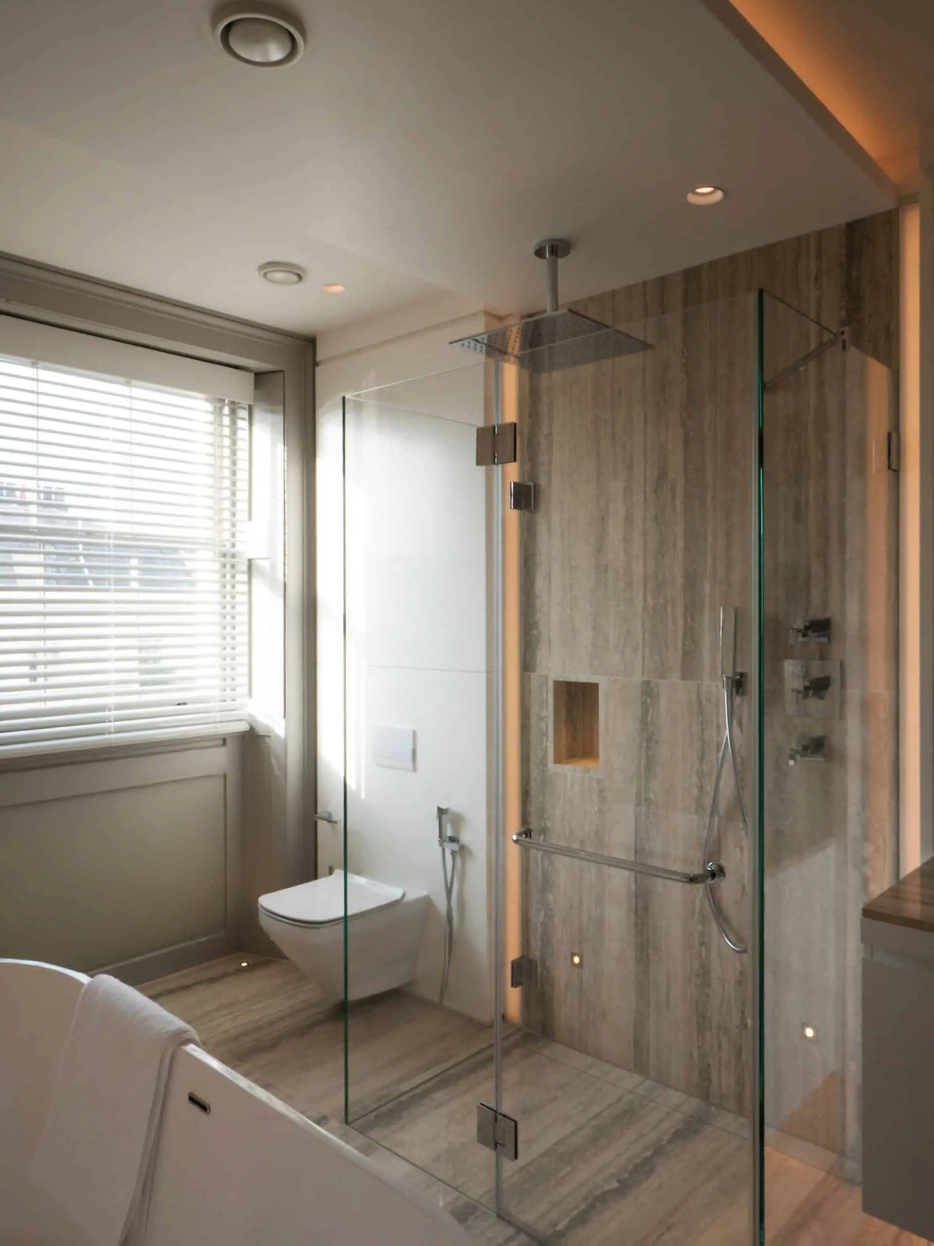 Minimalist stone bathroom with glass partitions and sleek modern fixtures.